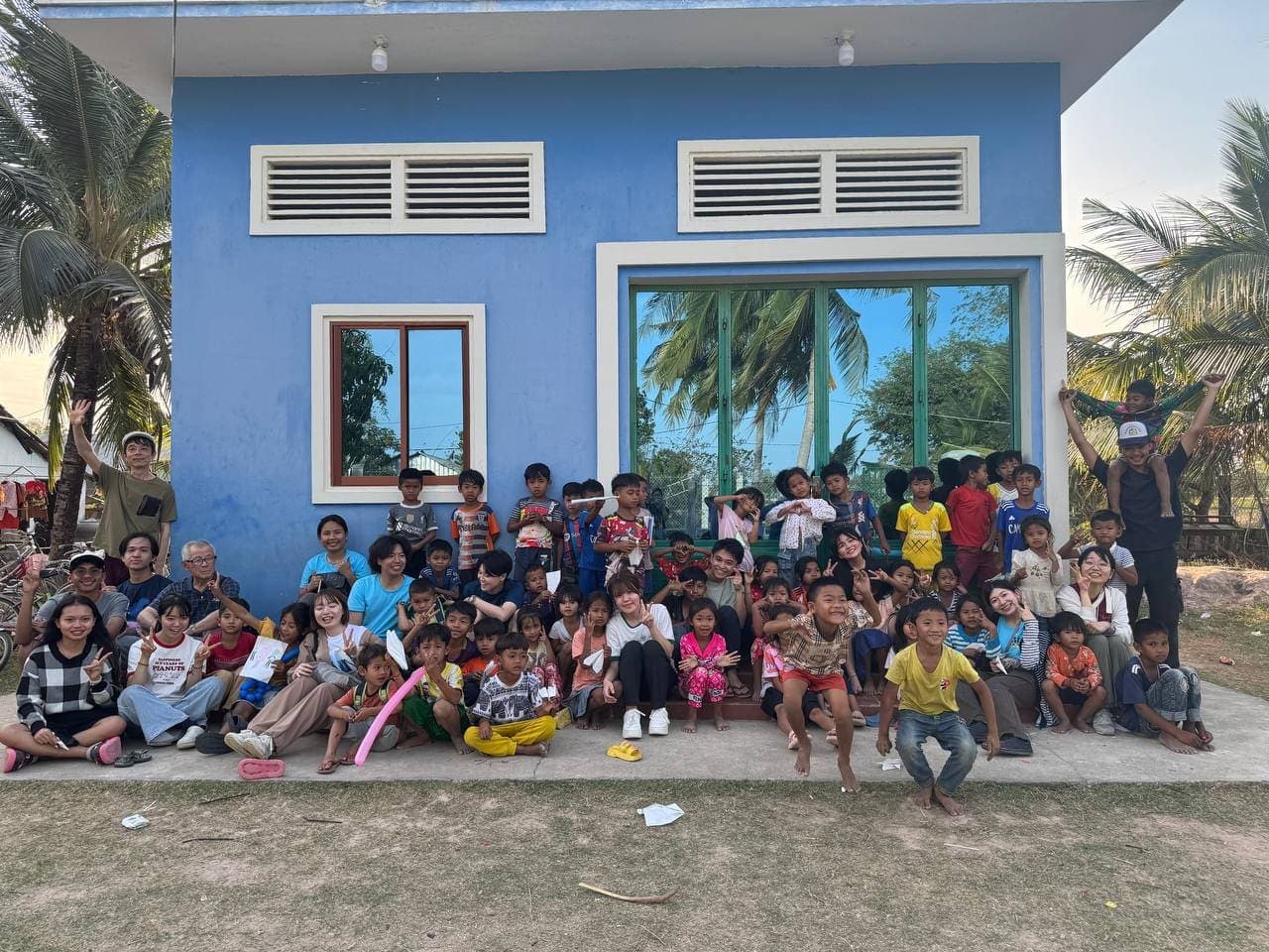 Volunteers and village children in front of a blue schoolhouse