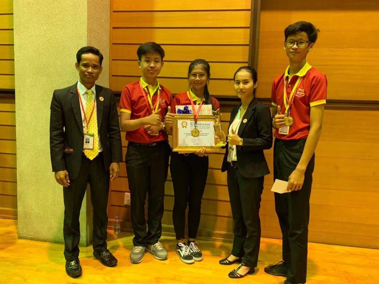 The winning team holding medals, a trophy and a framed certificate with their coaches
