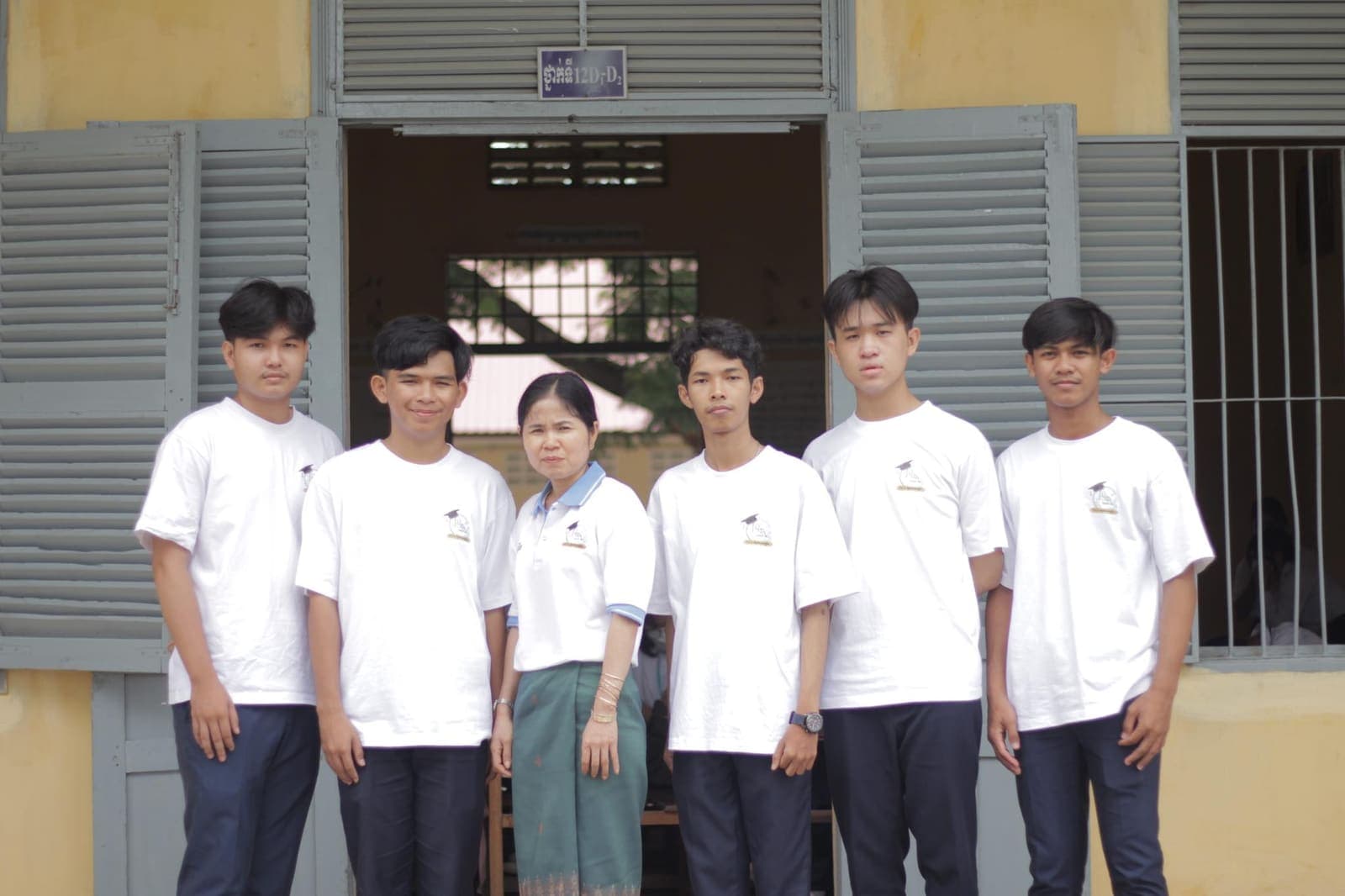 A group of high school classmates and a teacher outside their classroom