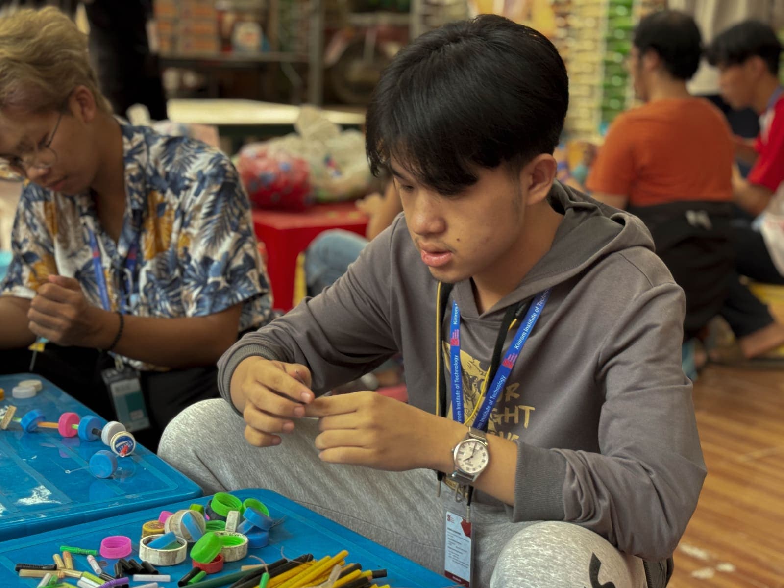 A volunteer threading bottle caps and straws into a souvenir
